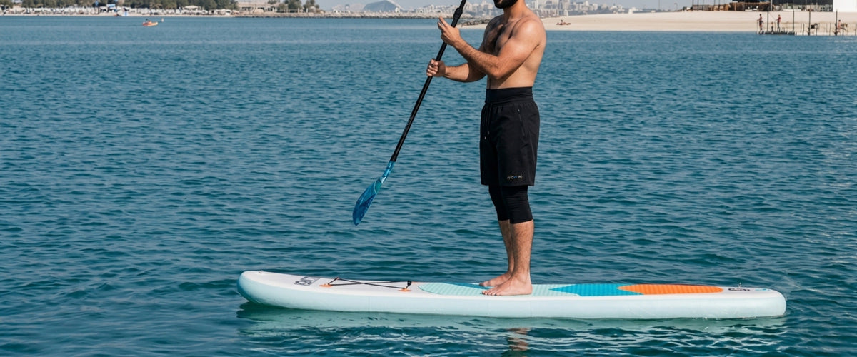Man standing on paddle board wearing the mawwj Awrah shorts